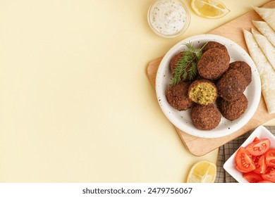 Plate with delicious falafel balls, tomatoes, sauce and pita on beige background