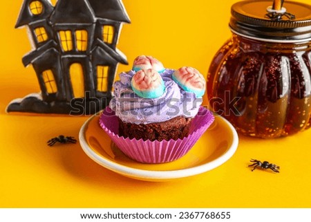 Plate with delicious Halloween cupcake, glass of cocktail and house on orange background, closeup