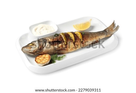 Plate with delicious roasted sea bass fish, garlic, slice of lemon and sauce on white background