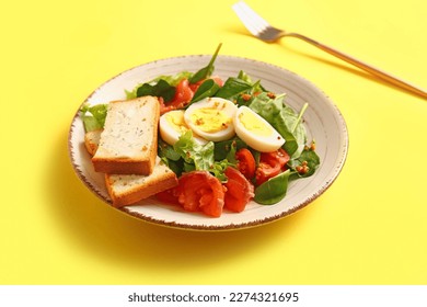 Plate of delicious salad with boiled eggs and salmon on yellow background