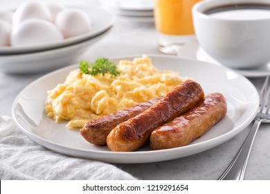 A plate of delicious scrambled eggs and breakfast sausage with coffee and orange juice.