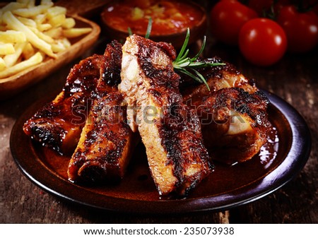 Plate of delicious spicy marinated grilled or barbecued spare ribs served with French Fries and tomato at a steakhouse or restaurant, close up view