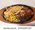 A plate of delicious steak served on a black plate with side dishes such as beans, carrots, corn and black pepper sauce which really increases the appetite on white background