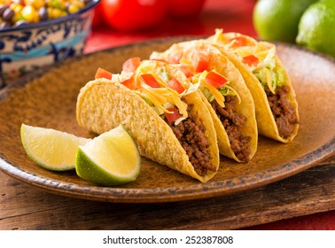 A plate of delicious tacos with lime, tomato, lettuce, and cheese.