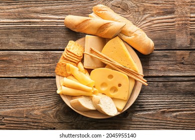 Plate with different types of cheese, bread and snacks on wooden background