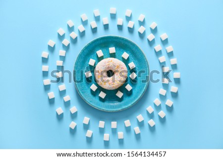 Plate with doughnut and sugar on color background