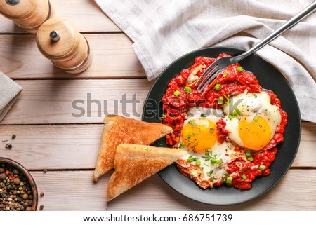 Plate with eggs in purgatory on wooden background