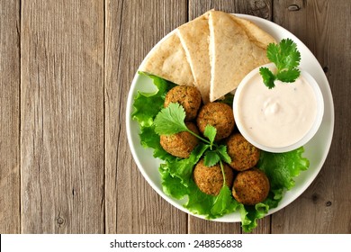 Plate Of Falafel With Pita Bread And Tzatziki Sauce On Wooden Table. View From Above