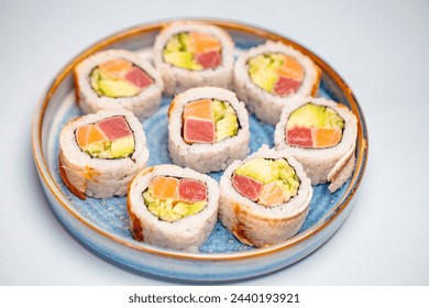 A plate filled with a variety of delicious sushi rolls and sashimi, placed on a pristine white table. - Powered by Shutterstock