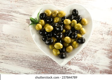 Plate in the form of heart with black and green olives on painted wooden background