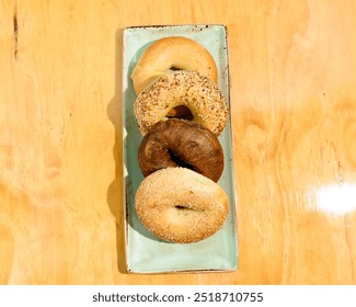 A plate of four assorted bagels sits on a wooden surface, showcasing a variety of textures and toppings. - Powered by Shutterstock