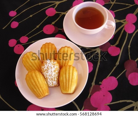 Plate of French madeleines with cup of tea in vintage dishware on black and pink cherry-patterned tablecloth Stock photo © 
