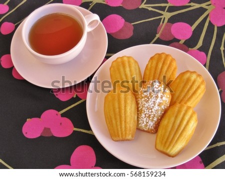 Plate of French madeleines with cup of tea in pink vintage dishware on elegant black and pink cherry-patterned tablecloth Stock photo © 