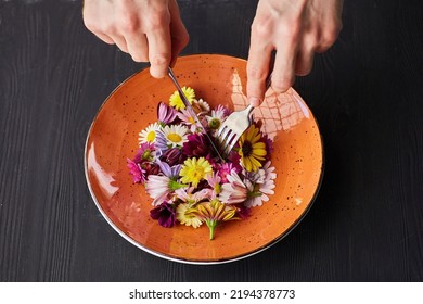 A Plate Of Fresh Flowers And Men's Hands. The Concept Of Plant-based Nutrition, Vegetarianism And Organic Food. Humor About The Lack Of Normal Food.