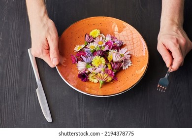 A Plate Of Fresh Flowers And Men's Hands. The Concept Of Plant-based Nutrition, Vegetarianism And Organic Food. Humor About The Lack Of Normal Food.