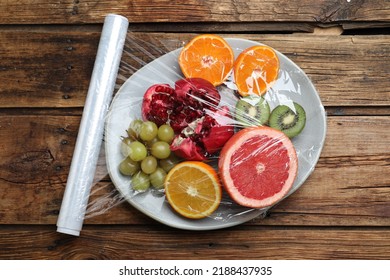 Plate Of Fresh Fruits With Plastic Food Wrap On Wooden Table, Flat Lay