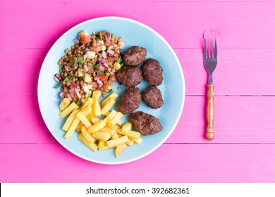 Plate Of Fresh Homemade Spicy Traditional Turkish Kofta Meatballs Served With A Fresh Lentil Salad And Fried Potato Chips Served On A Vibrant Pink Picnic Table, Overhead View
