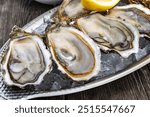 Plate with fresh live raw oysters seashells with citron, bread, butter and white wine served on ice at restaurant in oyster-farming village, Arcachon bay, Gujan-Mestras port, France