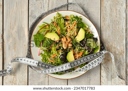 Plate with fresh salad and measure tape on grey wooden background. Diet concept