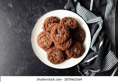 Plate Of Fresh Salted Dark Chocolate Cookies On Black Slate Counter.