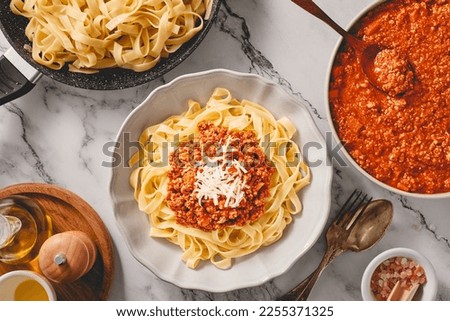 Plate of fresh tagliatelle pasta with bolognese sauce and bowl of fresh BOLOGNESE SAUCE and a pan of cooked tagliatelle pasta. Top view.