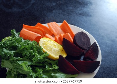 A plate of fresh vegetables for juice mix. The plate contains vibrant green kale leaves, bright orange carrot sticks, deep red beetroot, and a half lemon. Selective focus - Powered by Shutterstock