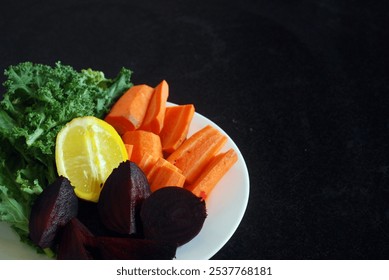 A plate of fresh vegetables for juice mix. The plate contains vibrant green kale leaves, bright orange carrot sticks, deep red beetroot, and a half lemon. Selective focus - Powered by Shutterstock