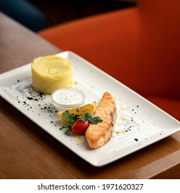 Plate with fried salmon fillet, lemon, sauce and mashed potatoes on restaurant table. Sea food concept. Nice serving dish. Square format or 1x1. Copy space.