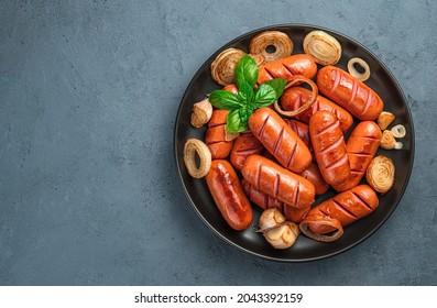 A plate of fried sausages with onions, garlic and basil on a dark gray background. Top view, space for copying.