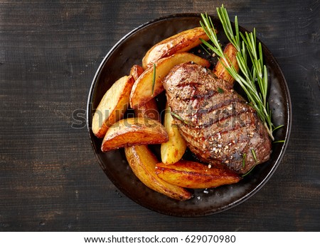 plate of grilled beef steak and potatoes on dark table, top view