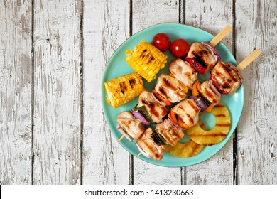 Plate Of Grilled Chicken Kabobs, Corn, And Pineapple. Top View On A White Wood Background. Summer BBQ Or Picnic Food Concept. 