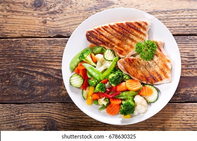 Plate Of Grilled Chicken With Vegetables On Wooden Table, Top View