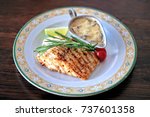 A plate of grilled escolar fish with creamy sauce on a rustic wooden table.