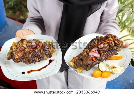 a plate of grilled ribs or ribs barbecue (iga bakar) held by a woman's hand