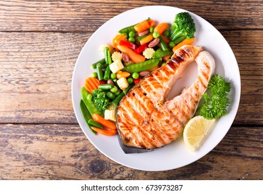plate of grilled salmon steak with vegetables on wooden table, top view