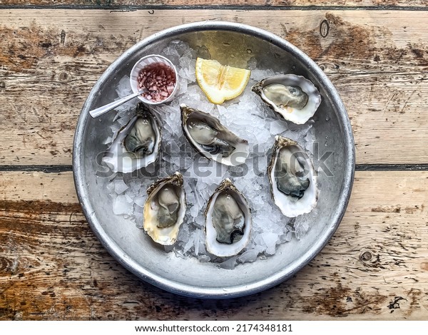 plate with half\
dozen of fresh oysters lemon wedges on wooden background cracked\
ice. Oyster. Rock native\
oysters.