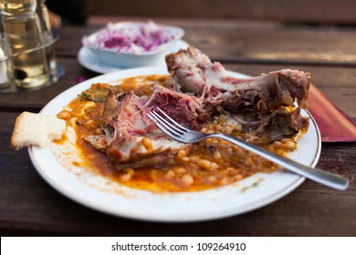 A Plate With Half Eaten Pork Shank With Beans