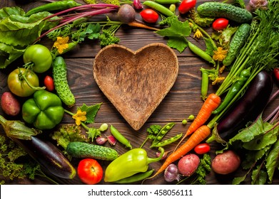 Plate Heart Shape Surrounded With Fresh Organic Vegetables On Wooden Background. Healthy Vegetarian Food, View From Above.