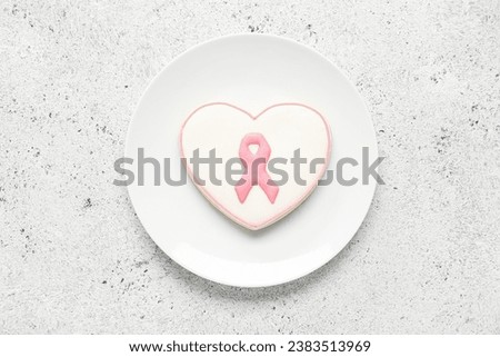 Plate with heart shaped cookie with pink ribbon on light grunge background. Breast cancer awareness concept