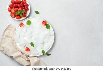 A plate of ice cubes and strawberries with mint on a gray background. Top view, copy space.