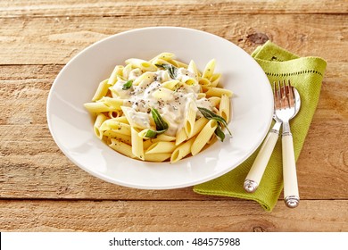 Plate Of Italian Penne Pasta Topped With A Formaggio Creamy Savory Sauce And Basil Served In A White Dish On A Rustic Wood Table