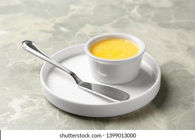 Plate with knife and bowl of clarified butter on grey background