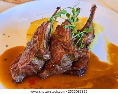 A plate of lamb chops served with mashed potatoes and a rich, brown gravy. The chops are cooked to a medium-rare and garnished with fresh herbs.