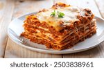 a plate of lasagna with layers of bolognese meat sauce and cheese, with basil leaves served on a white plate