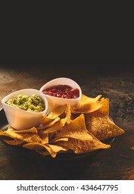 Plate Of Mexican Cuisine Appetizer Of Triangular Yellow Corn Tortilla Chips Beside Little Bowls Of Guacamole And Salsa Dip