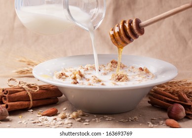 Plate of muesli with pouring milk and honey, cinnamon and nuts over textile background - Powered by Shutterstock