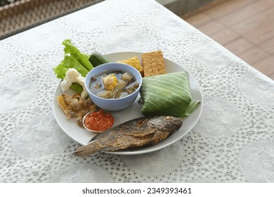 A plate of nasi timbel on the table. Nasi timbel wrapped on banana leaf, fried tilapia fish, salted fish, fried tempeh and tofu, raw vegetables and paste chili. Traditional food from Indonesia.  - Shutterstock ID 2349393461