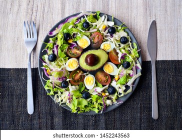 Plate on a burlap cloth background with keto food:quail eggs,cherry tomatoes,
avocado,olive oil,berries,spinach.
Ketogenic low carbs diet concept,top 
view.Healthy fats,clean eating for weight loss.