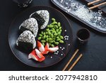 Plate with onigiri or japanese rice balls, crab meat and edamame, high angle view on a black stone background, horizontal shot