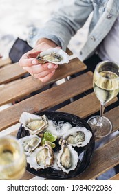 A plate of oysters, two glasses of white wine on a wooden table in a bar. Man holding an oyster 